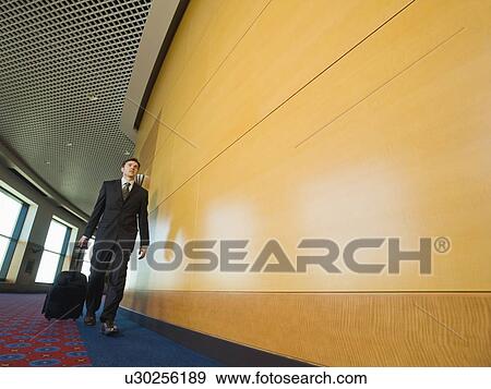Stock Photo - Businessman pulling suitcase in office corridor. Fotosearch