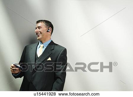 Stock Photo - Businessman using cell phone and hands-free device. Fotosearch