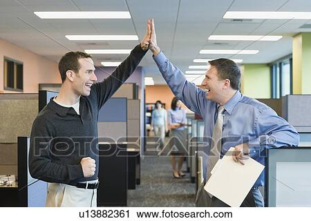 Stock Image - Businessmen high-fiving in office. Fotosearch
