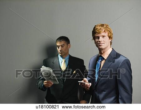 Stock Image - Businessmen holding newspaper and cell phone. Fotosearch