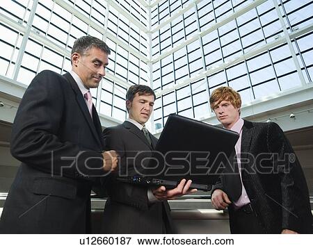 Businessmen looking at laptop in convention center atrium View Large Photo Image Stock Photo - Businessmen looking at laptop in convention center atrium. Fotosearch