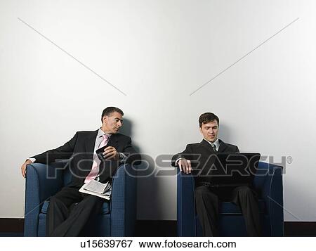 Stock Photo - Businessmen sitting in chairs in office lobby. Fotosearch