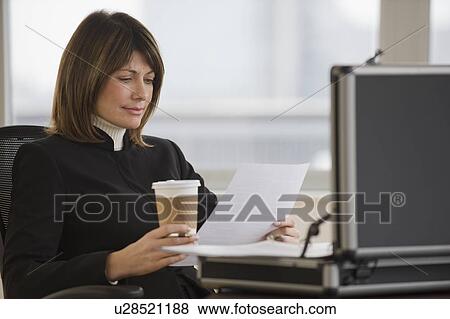Businesswoman holding coffee and reading paperwork View Large Photo Image Stock Photo - Businesswoman holding coffee and reading paperwork. Fotosearch