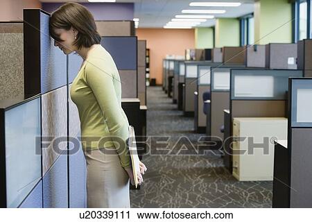 Stock Image - Businesswoman leaning head on cubicle wall. Fotosearch