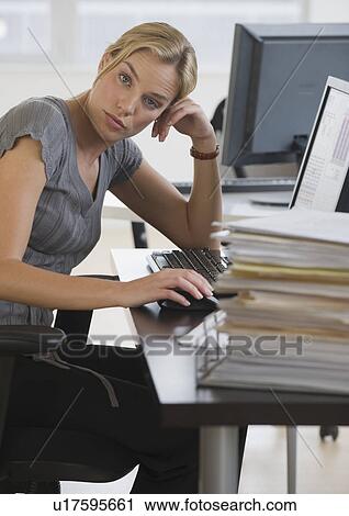 Stock Image - Businesswoman with stack of paperwork on desk. Fotosearch