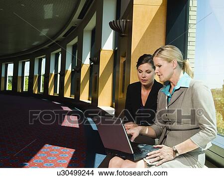 Businesswomen looking at laptop in office corridor View Large Photo Image Picture - Businesswomen looking at laptop in office corridor. Fotosearch