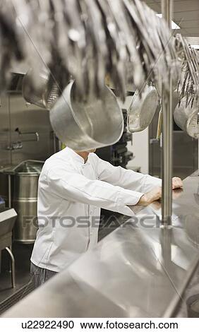 Stock Image - Chef leaning on shelf in commercial kitchen. Fotosearch