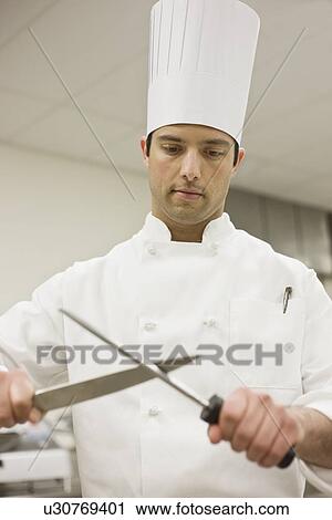Stock Image - Chef sharpening knife in kitchen. Fotosearch