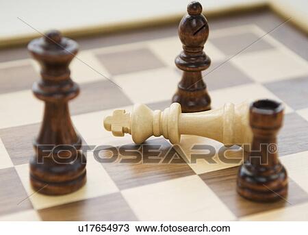 Stock Image - Chess pieces surrounding fallen king. Fotosearch