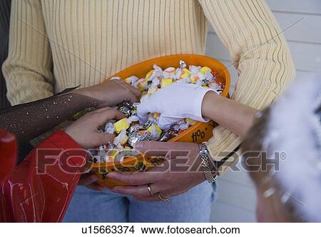 Picture - Children in Halloween costumes reaching into bowl of candy. Fotosearch