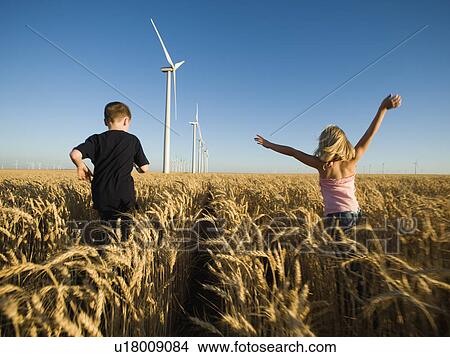 Picture - Children running through tall wheat field on wind farm. Fotosearch