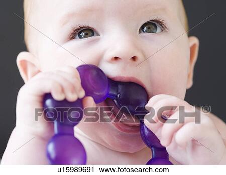 Stock Image - Close up of baby gnawing on teething ring. Fotosearch