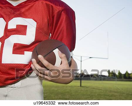 Stock Image - Close up of football player holding football on field. Fotosearch