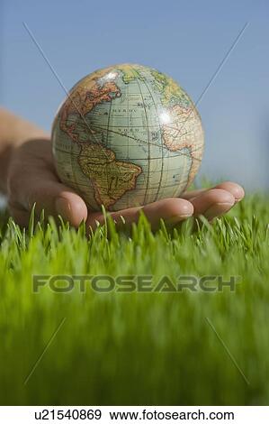 Stock Photo - Close up of hand holding globe in grass. Fotosearch
