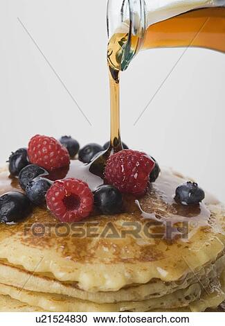 Stock Image - Close up of maple syrup being poured on pancakes. Fotosearch