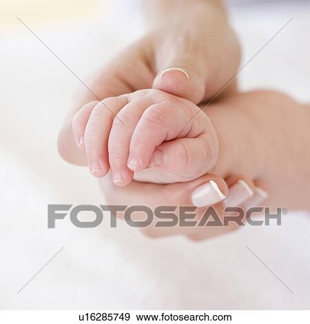 Stock Photo - Close up of mother holding baby’s hand. Fotosearch