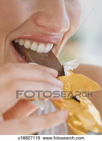 Stock Photo - Close up of woman biting chocolate bar. Fotosearch