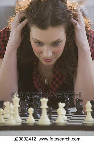 Stock Image - Close up of woman looking down at chessboard. Fotosearch