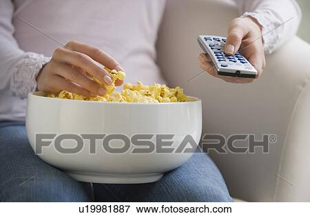 Stock Photo - Close up of woman with remote control and bowl of popcorn. Fotosearch