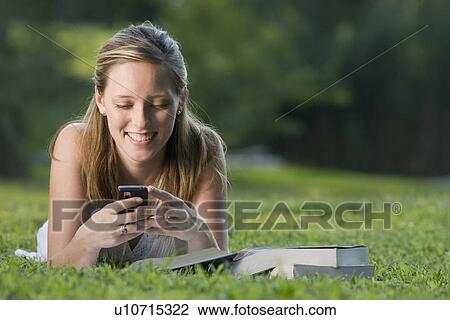 Stock Image - College student reading in grass and text messaging. Fotosearch