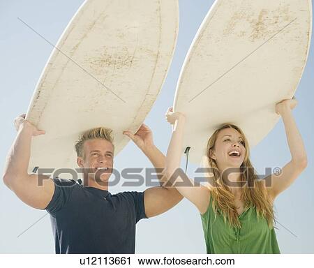 Stock Image - Couple holding surfboards on head. Fotosearch