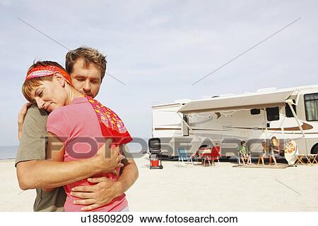 Stock Photo - Couple hugging on beach with motor home in background. Fotosearch