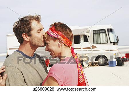 Stock Photo - Couple kissing by motor home on beach. Fotosearch