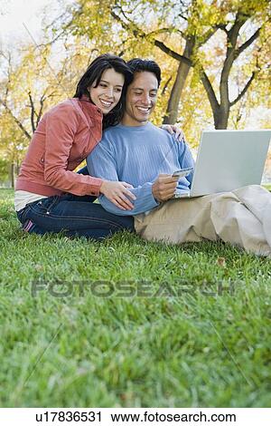 Couple looking at laptop in grass View Large Photo Image Stock Image - Couple looking at laptop in grass. Fotosearch