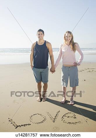 Couple next to Love written in sand View Large Photo Image Stock Photo - Couple next to Love written in sand. Fotosearch