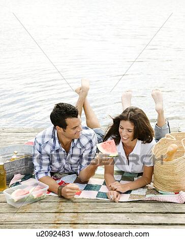 Stock Image - Couple picnicking on dock. Fotosearch