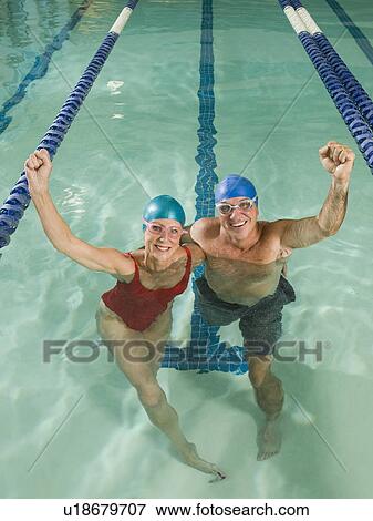 Stock Photo - Couple posing in swimming pool with arms raised. Fotosearch