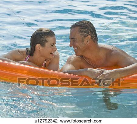 Stock Image - Couple resting on raft in swimming pool. Fotosearch