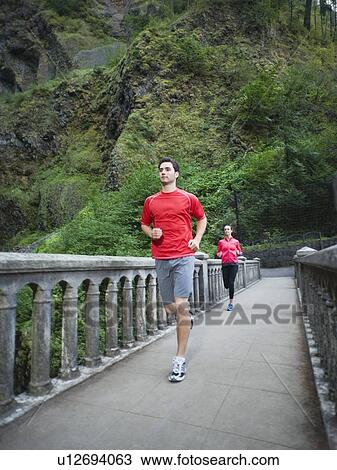 Stock Image - Couple running across bridge. Fotosearch