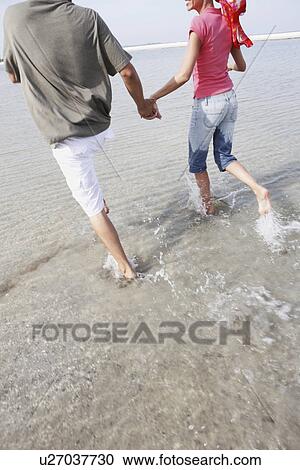 Stock Image - Couple running in ocean. Fotosearch