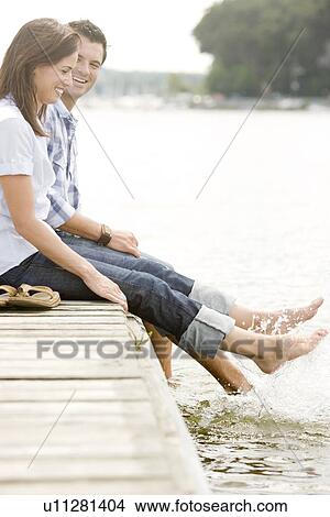 Picture - Couple sitting on dock and splashing feet in lake. Fotosearch