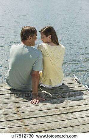 Stock Image - Couple sitting on dock. Fotosearch