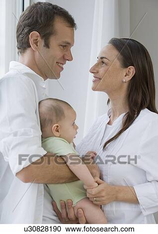 Stock Image - Couple standing face to face holding baby son. Fotosearch