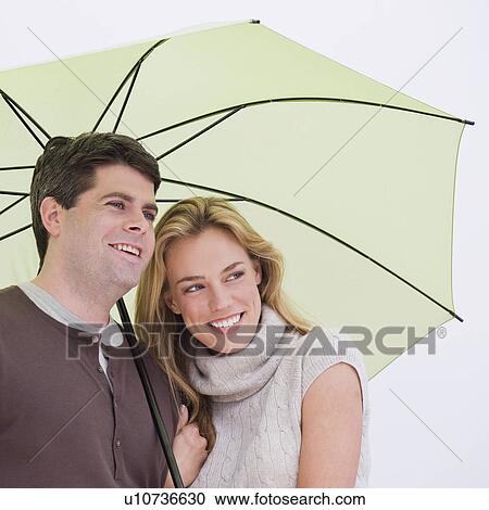 Stock Image - Couple standing under umbrella. Fotosearch