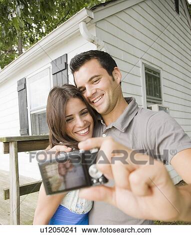 Couple taking self-portrait in front of house View Large Photo Image Stock Image - Couple taking self-portrait in front of house. Fotosearch