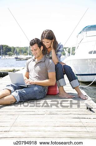 Stock Photo - Couple using laptop on dock. Fotosearch