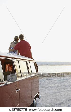 Couple watching ocean sunset from top of van View Large Photo Image Stock Photograph - Couple watching ocean sunset from top of van. Fotosearch