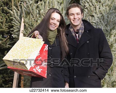 Picture - Couple with shopping bags in front of Christmas trees. Fotosearch