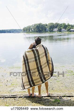 Couple wrapped in blanket looking out at lake View Large Photo Image Stock Photo - Couple wrapped in blanket looking out at lake. Fotosearch