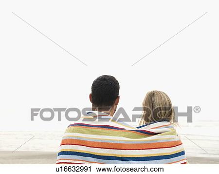 Stock Image - Couple wrapped in towel on beach. Fotosearch
