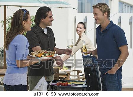Stock Image - Couples barbecuing on patio. Fotosearch