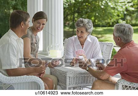 Stock Image - Couples playing card game on porch. Fotosearch