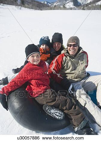 Stock Photograph - Family sitting on tube in snow. Fotosearch
