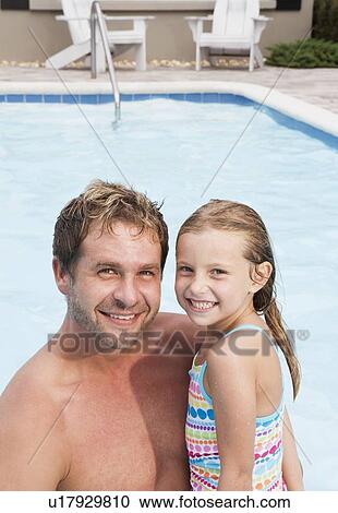 Stock Image - Father and daughter posing by swimming pool. Fotosearch