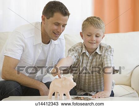 Stock Image - Father and son putting money in piggy bank. Fotosearch