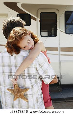 Stock Photograph - Father carrying sleepy daughter and starfish to motor home. Fotosearch